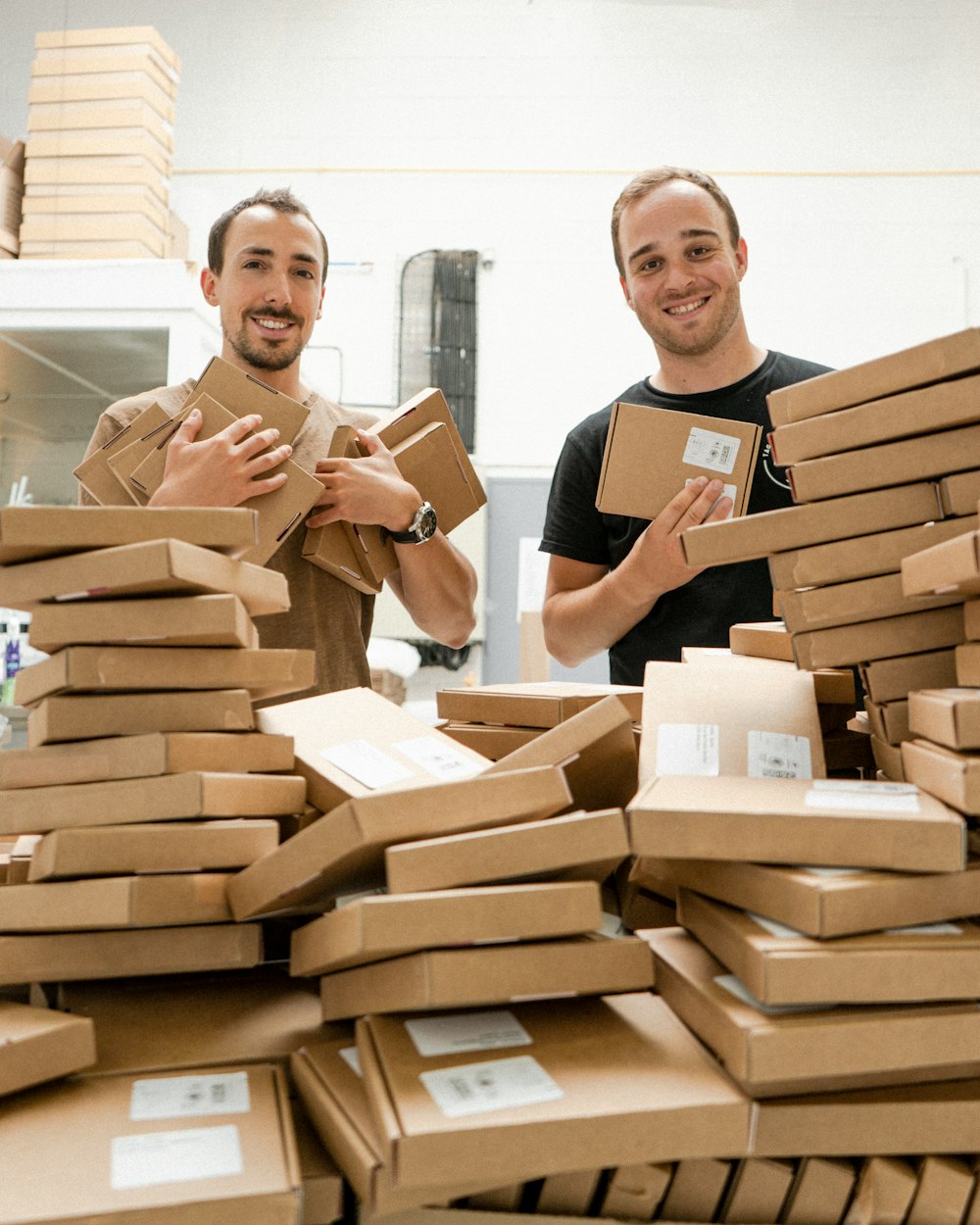 Two team members packing orders among stacks of boxes